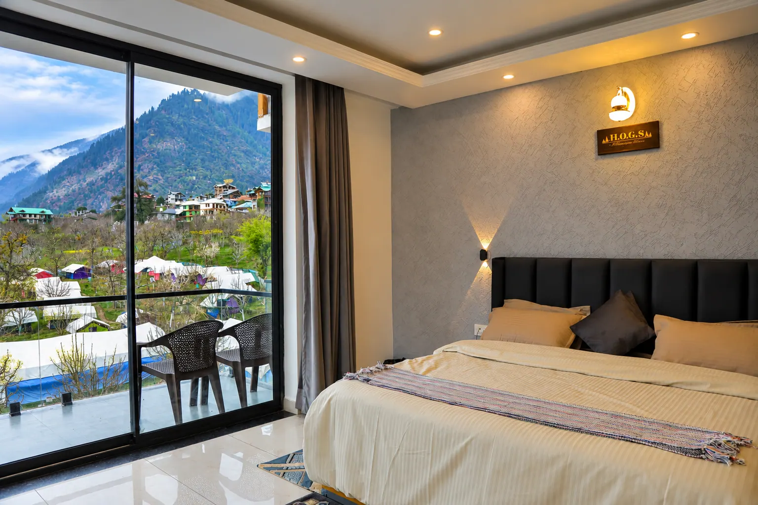 Cozy bedroom at HOGS Panorama, Manali, with warm lighting and floor-to-ceiling windows overlooking the valley